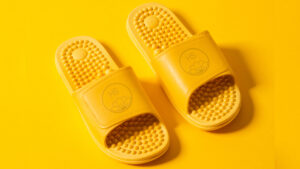 Pair of sundrop yellow PVC massaging sliders with textured footbed on a yellow background