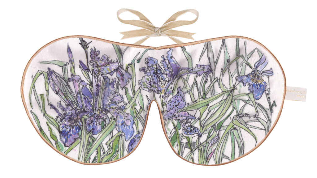 A silk sleep mask featuring a hand‑illustrated iris flower design in shades of purple and green with gold edging and ribbon ties.