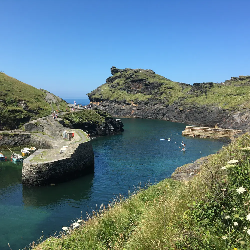 Harbour inlet surrounded by steep green cliffs with moored boats on calm blue water.